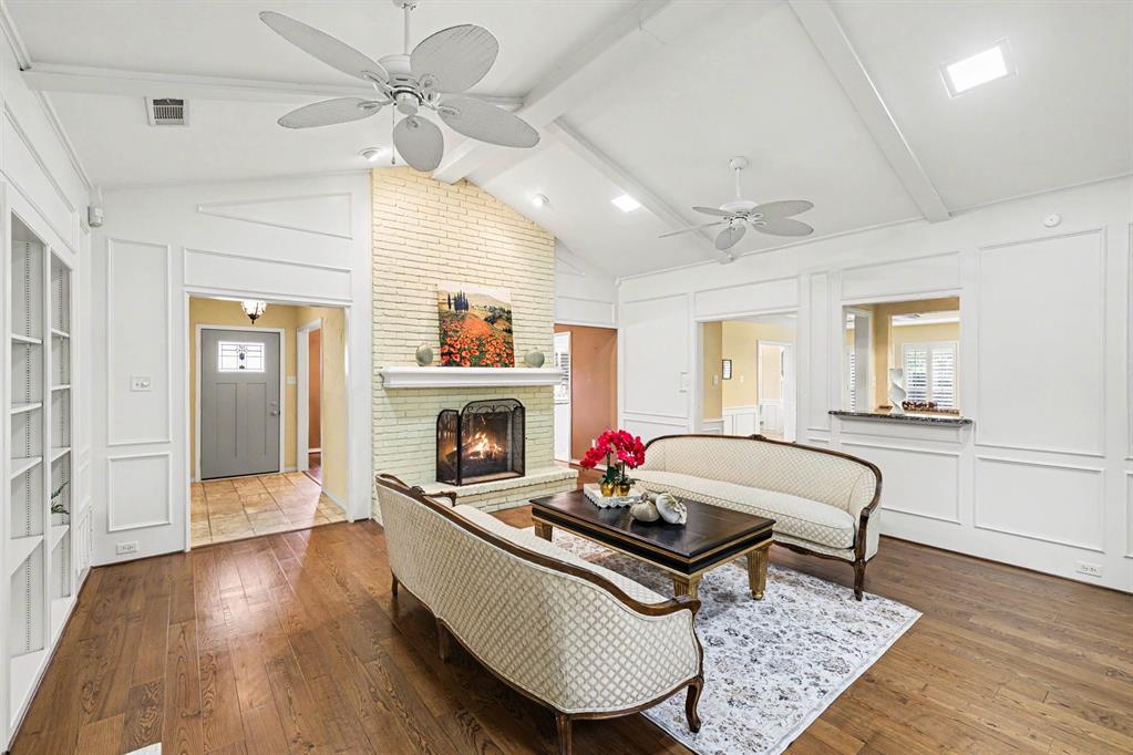 Vaulted ceiling with exposed beams, wood-finish flooring, brick fireplace with a mantel, built-in shelving, and transom windows Vaulted ceiling with exposed beams, wood-finish flooring, brick fireplace with a mantel, built-in shelving, and transom windows