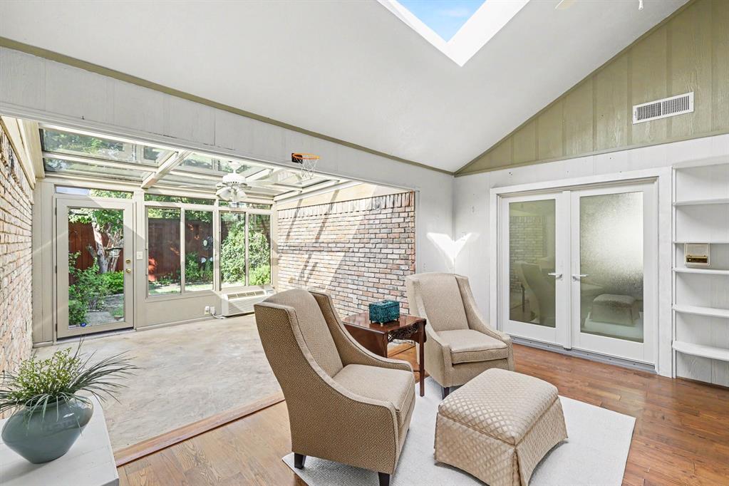 Vaulted ceiling with skylight, wood-finish flooring, built-in shelving, and frosted glass French doors