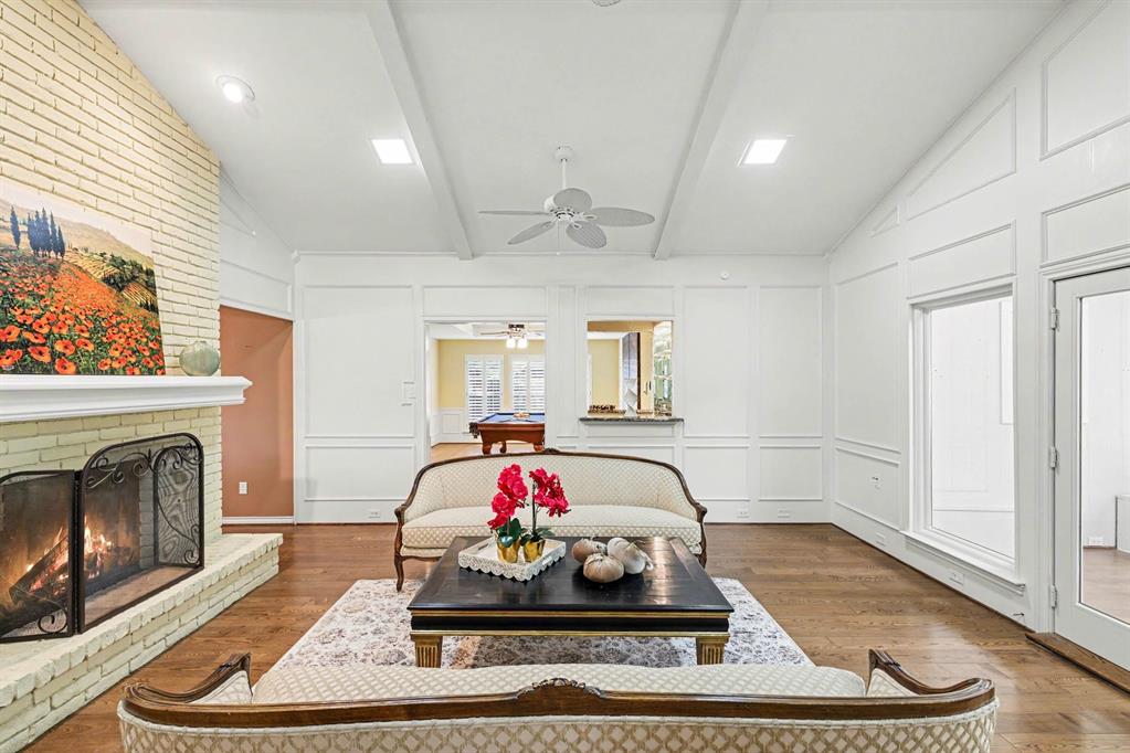 Vaulted ceiling with exposed beams, brick fireplace, wood-finish flooring, recessed lighting, and white wall paneling Vaulted ceiling with exposed beams, brick fireplace, wood-finish flooring, recessed lighting, and white wall paneling