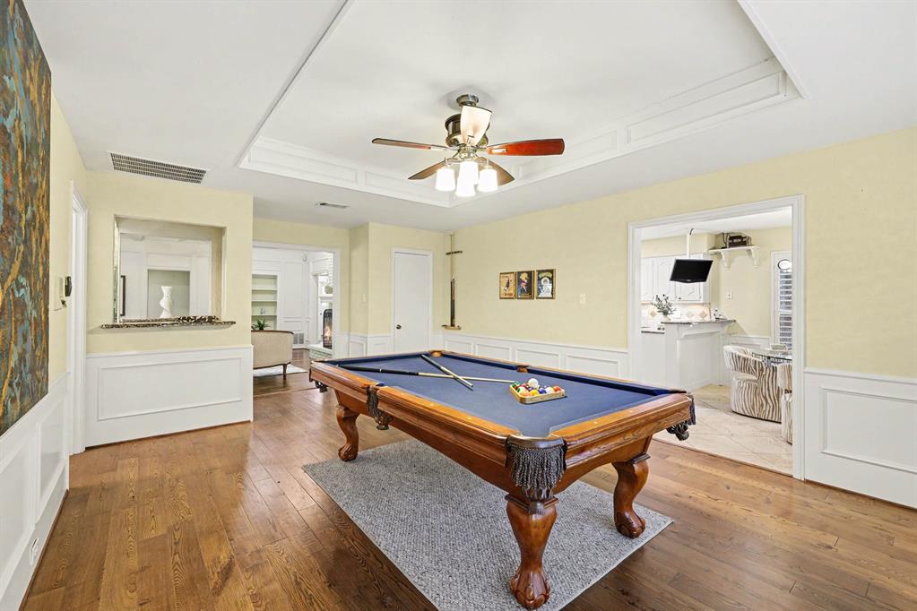 Wood-finish flooring throughout, tray ceiling with crown molding, ceiling fan with integrated lighting, and wainscoting on lower walls