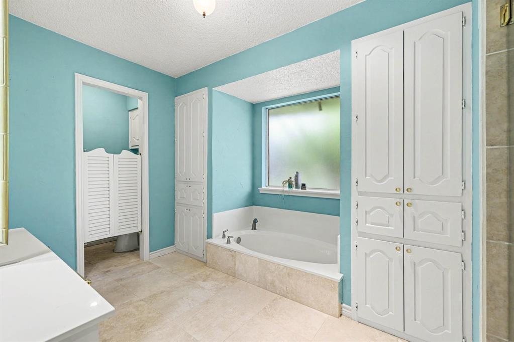 Built-in soaking tub with surrounding tile, large obscured window, multiple built-in storage cabinets, and tile flooring