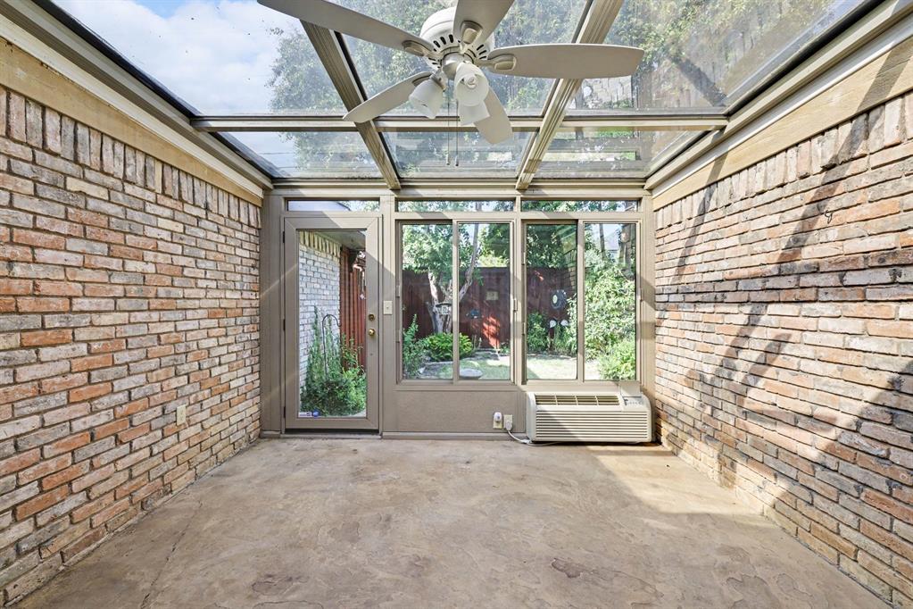Sunroom with a glass roof, exposed brick walls, a ceiling fan, and concrete flooring