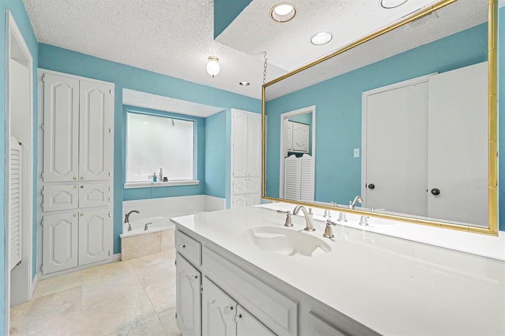 Dual vanity with integrated sink, white cabinetry, recessed lighting, built-in soaking tub, and tile flooring