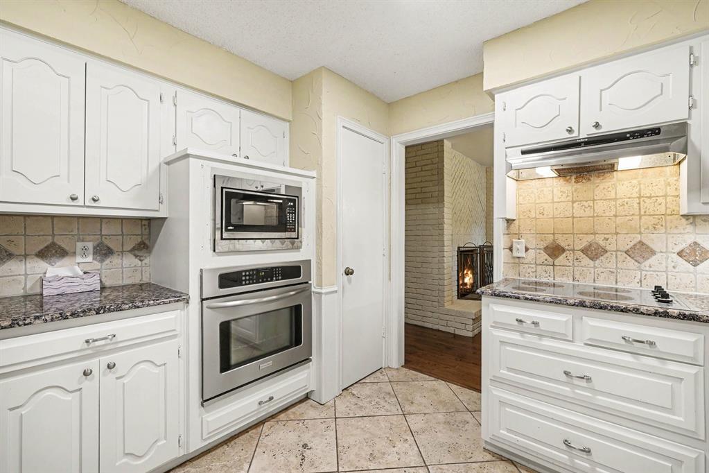 White cabinetry with decorative fronts, stainless steel built-in appliances, tiled flooring, speckled countertops, and a tiled backsplash