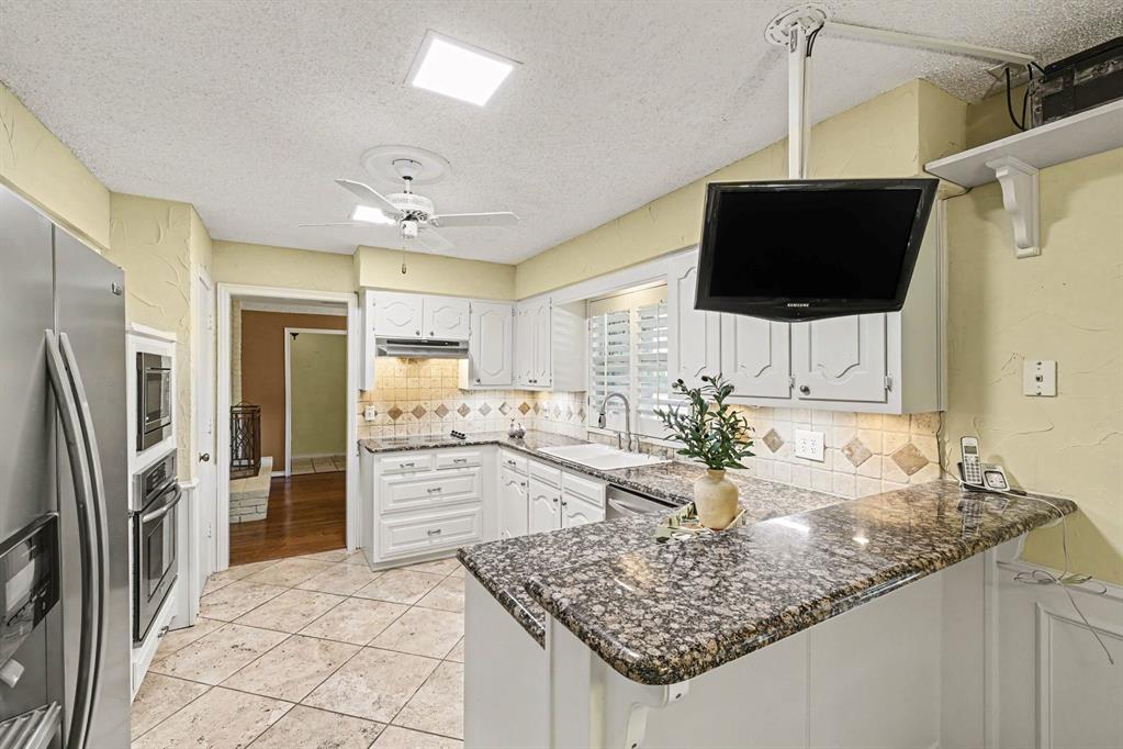 Kitchen featuring white cabinetry, granite countertops, tile backsplash, built-in stainless steel appliances, and a ceiling fan
