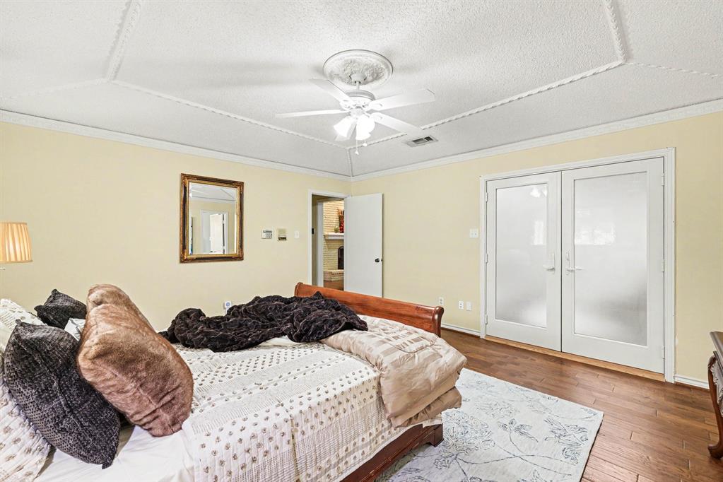 Wood-finish flooring, white double doors with frosted glass, ceiling fan with light fixture, decorative ceiling trim, and light yellow wall color