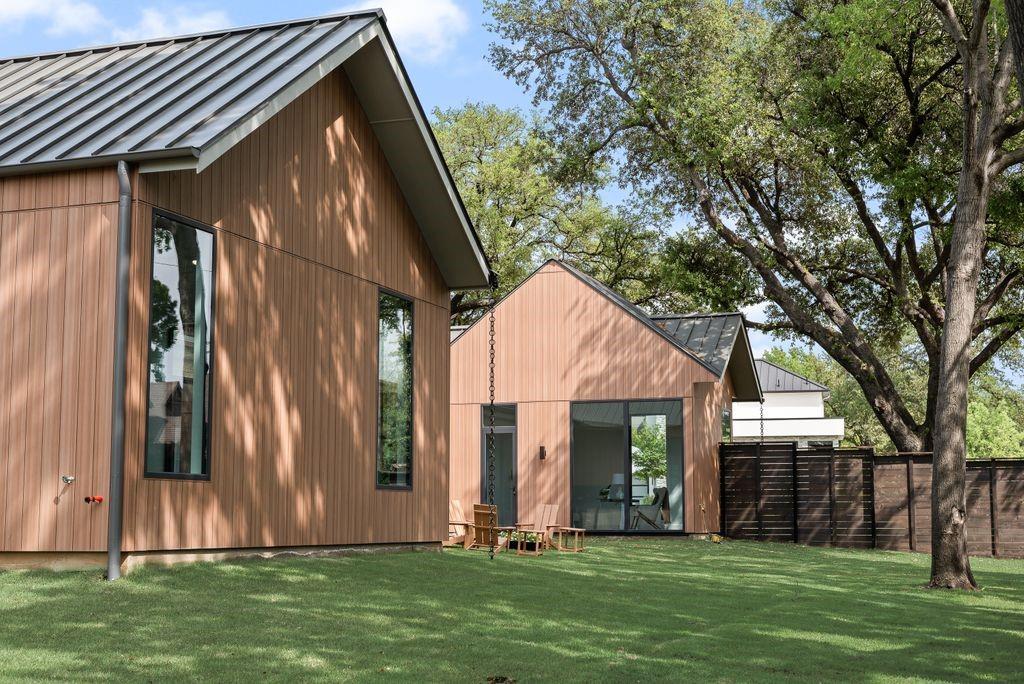 Board and batten siding in natural tones complements the wood-stained fence and mature trees, creating a warm and inviting exterior.
