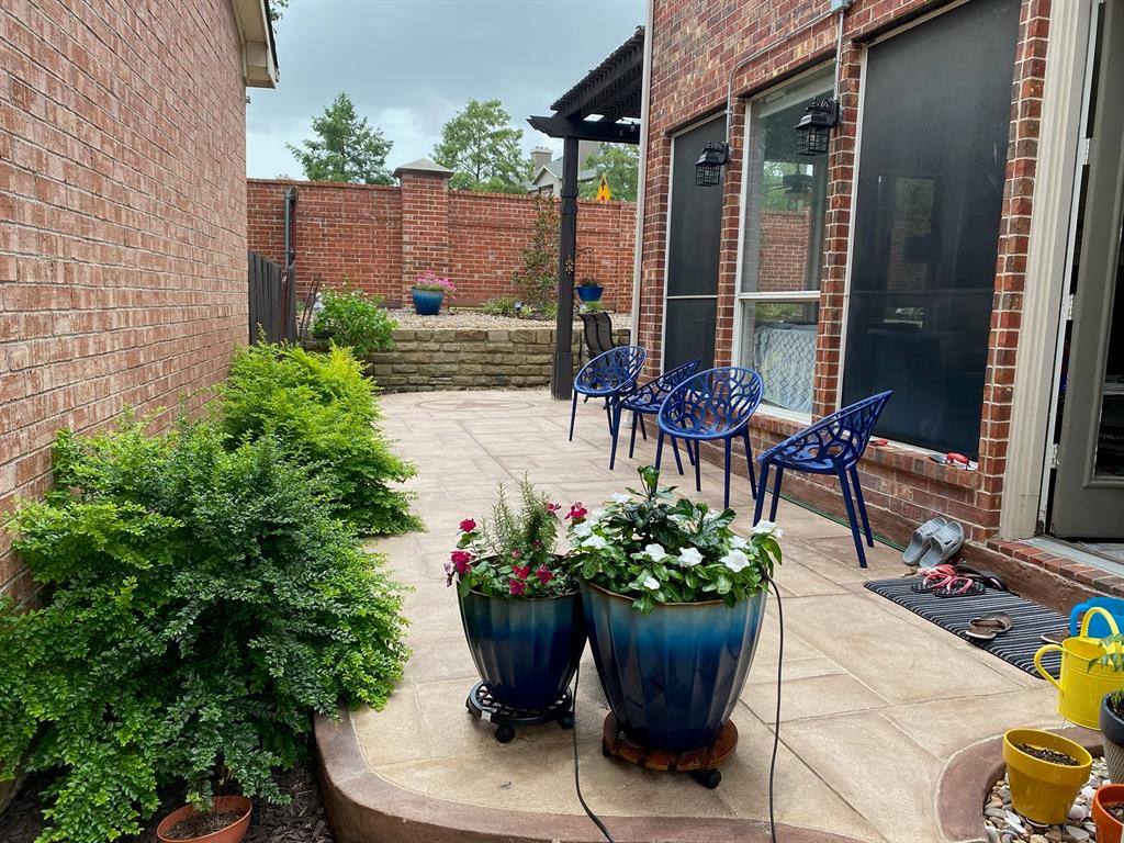 Paved patio area, brick exterior, built-in wall sconces, terraced landscaping, and mature shrubbery