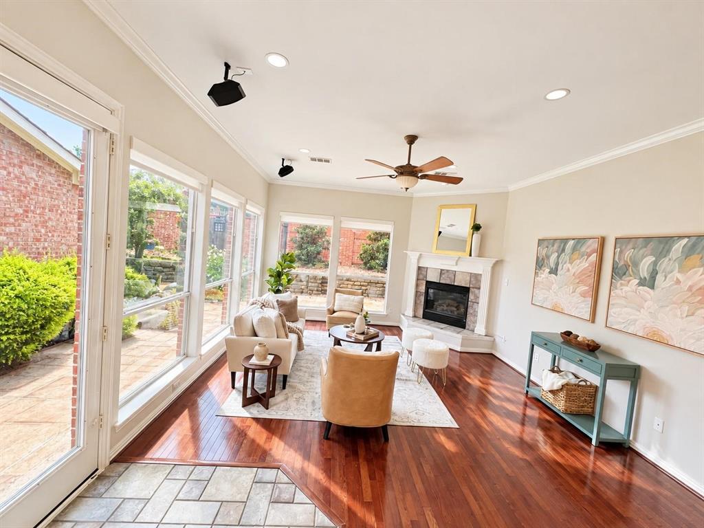 Rich wood-finish flooring, stone-surround fireplace, ceiling fan, and extensive window system overlooking an exterior patio