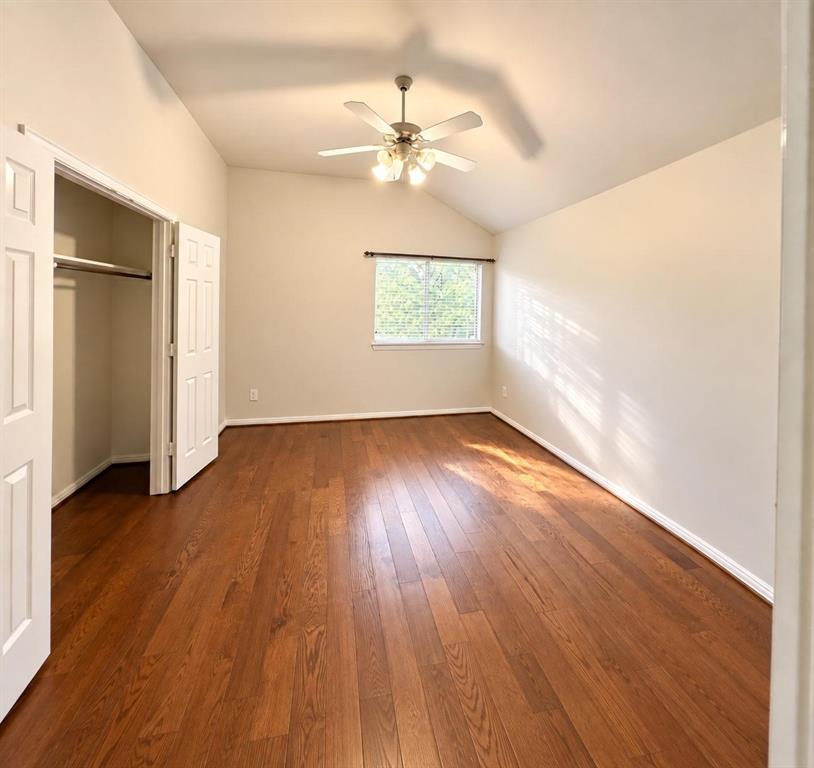 Vaulted ceiling with a ceiling fan, wood-finish flooring, window with blinds, and a closet with bifold doors