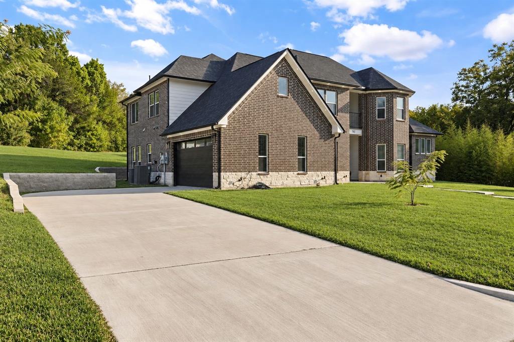 Brick exterior with stone accents, dark-paneled garage door, concrete driveway, lush green lawn, and mature trees