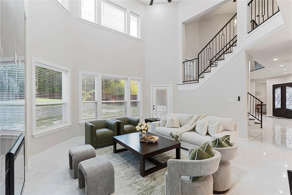 Two-story living area featuring a prominent staircase with black wrought iron balusters, multiple large windows, and high ceilings
