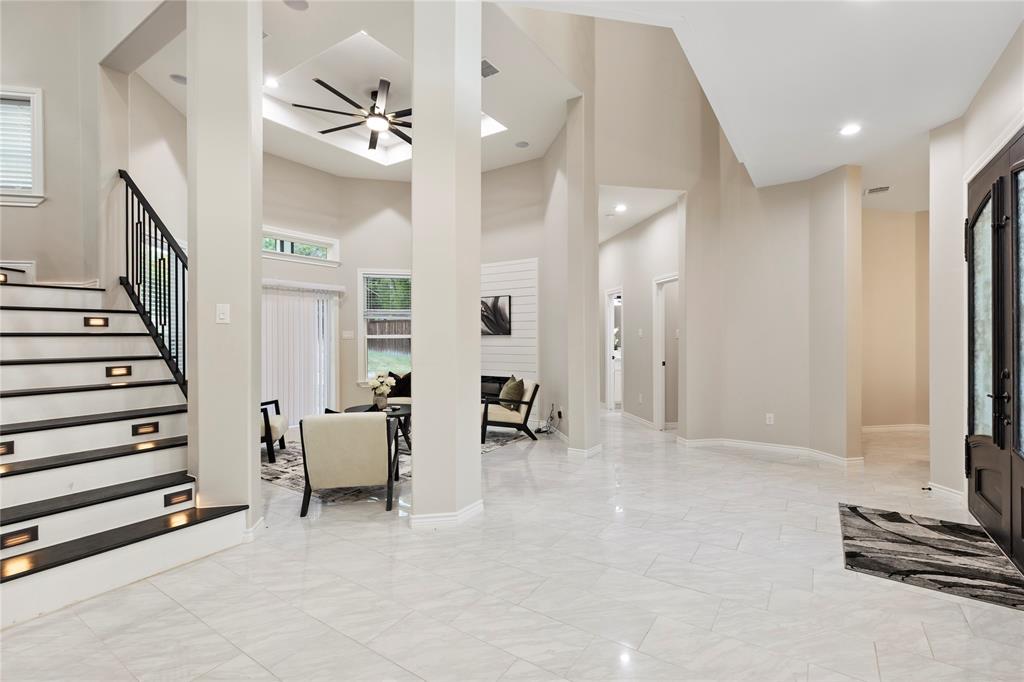 Vaulted ceiling with a ceiling fan, light-colored tile flooring, stairway with accent lighting, white shiplap fireplace, and a dark wood entry door Vaulted ceiling with a ceiling fan, light-colored tile flooring, stairway with accent lighting, white shiplap fireplace, and a dark wood entry door