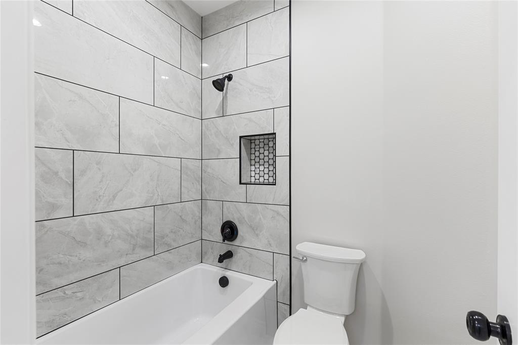 Bathtub with tiled surround, recessed shower niche, and matte black fixtures