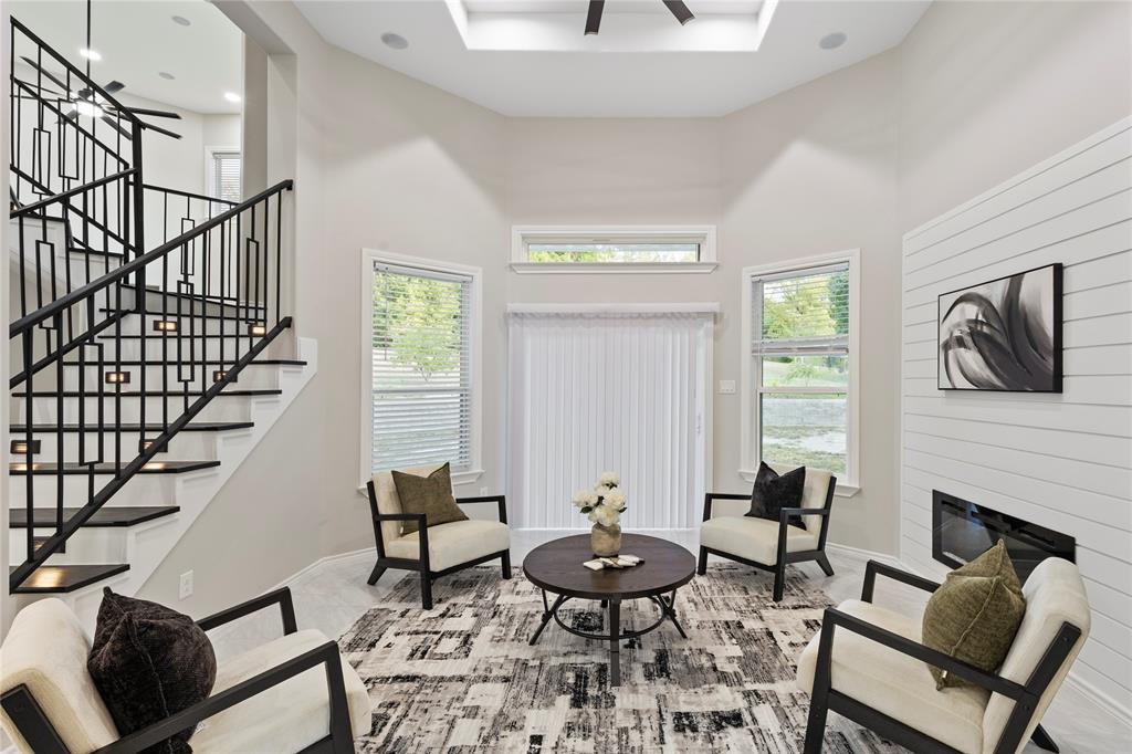 Vaulted ceiling with integrated lighting, contemporary black metal staircase with under-stair illumination, multiple windows with blinds, shiplap accent wall, and a built-in linear fireplace Vaulted ceiling with integrated lighting, contemporary black metal staircase with under-stair illumination, multiple windows with blinds, shiplap accent wall, and a built-in linear fireplace