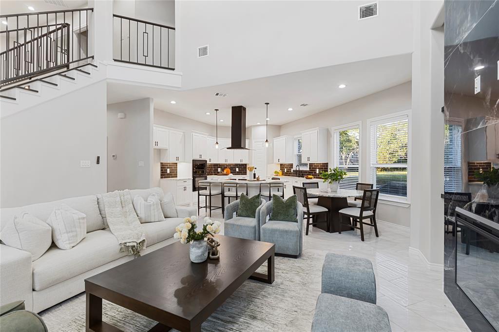 Two-story ceiling, open-concept design, built-in fireplace, large windows, and a kitchen island with seating