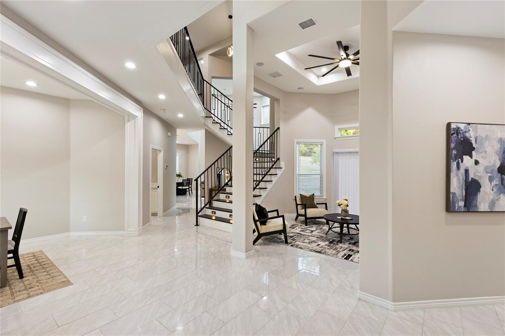 Spacious open-concept interior featuring light-toned flooring, a grand staircase with wrought-iron railings, a recessed ceiling with a fan, and recessed lighting throughout Spacious open-concept interior featuring light-toned flooring, a grand staircase with wrought-iron railings, a recessed ceiling with a fan, and recessed lighting throughout