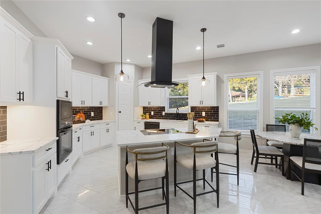 White cabinetry with black hardware, stone countertops, and a dark brick-patterned backsplash
