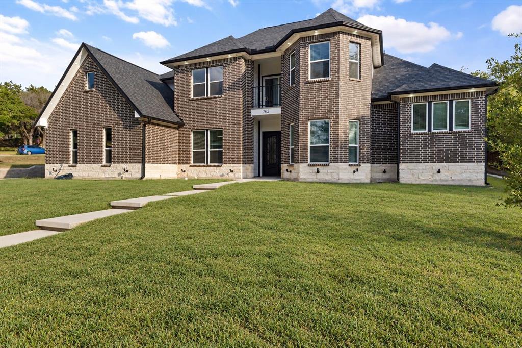 Two-story brick exterior with stone accents, multiple windows, a second-story balcony, and a prominent front entrance