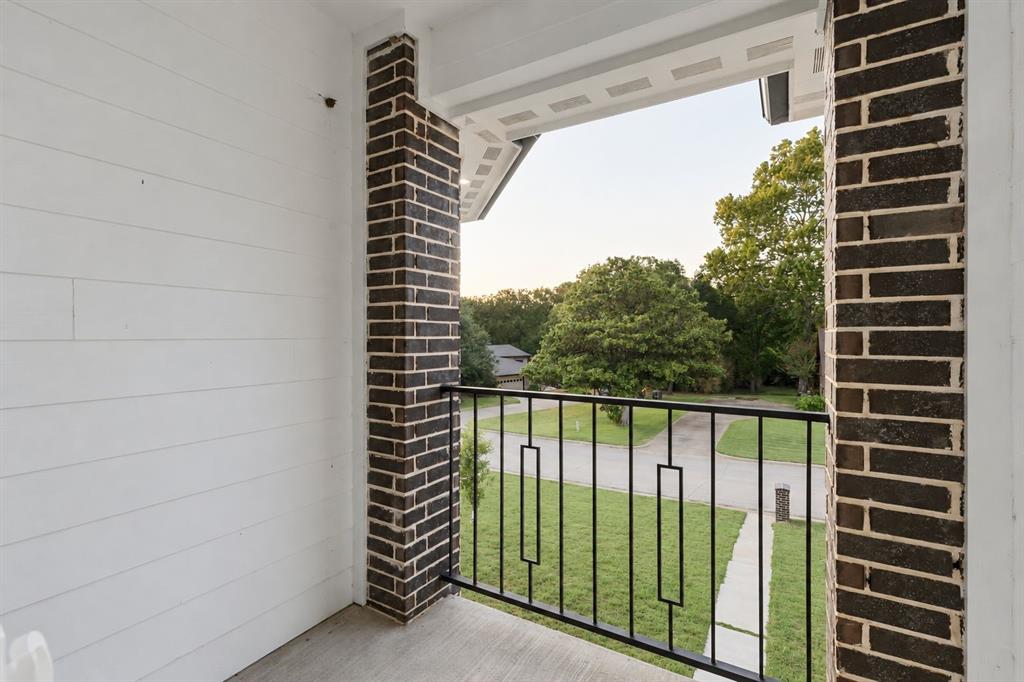 Balcony featuring dark brick columns, white horizontal siding, a black metal railing, and a concrete floor