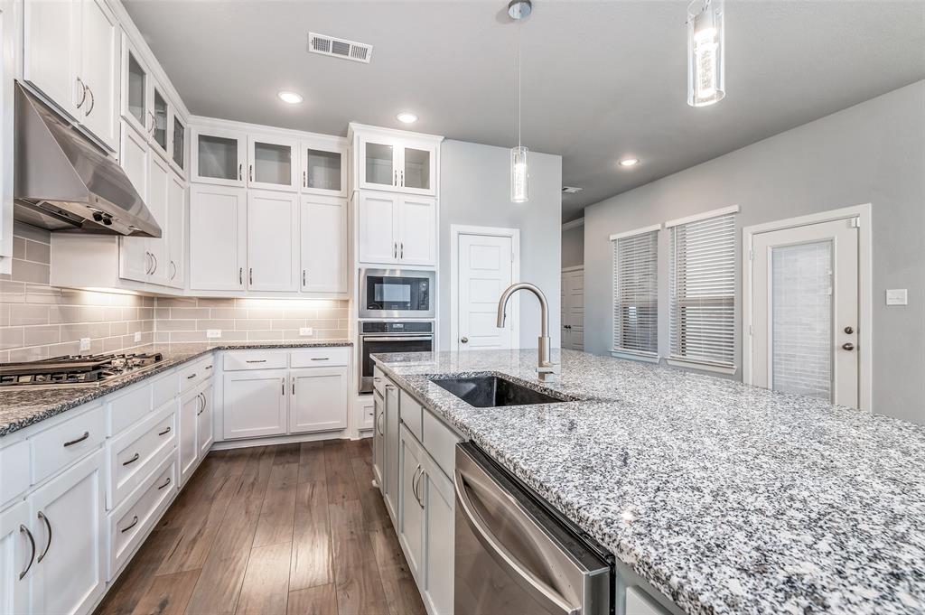 Kitchen featuring white shaker cabinetry, stainless steel appliances, granite countertops, wood-finish flooring, and a subway tile backsplash