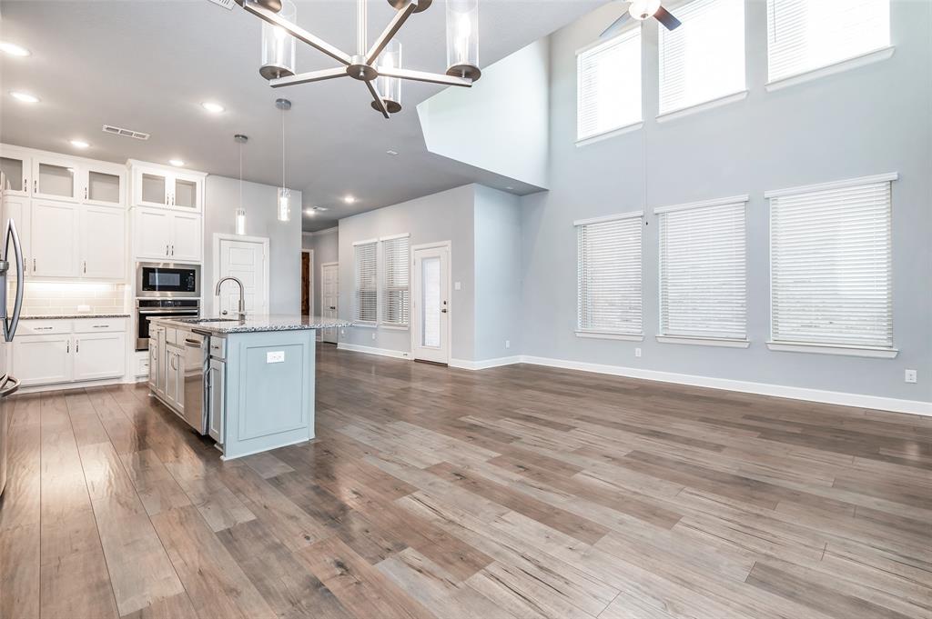 Open-concept living area with high ceilings, wood-finish flooring, a contemporary chandelier, and a kitchen island with pendant lighting