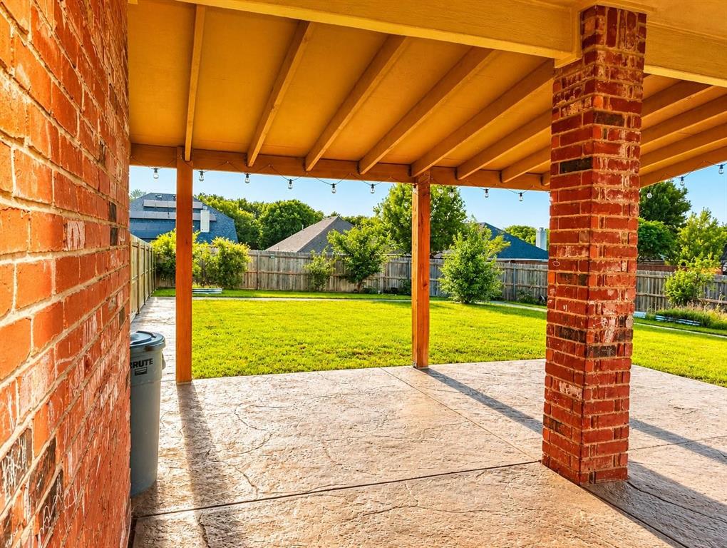 Covered patio featuring a stamped concrete surface, brick support columns, and a level lawn beyond