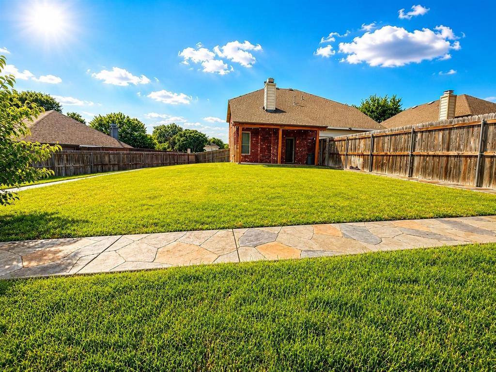 Expansive backyard featuring a lush lawn, stone-patterned walkway, and privacy fencing