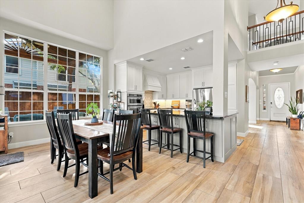 High-ceiling interior space featuring wood-finish flooring, white cabinetry, a kitchen island with stone-surface countertops, and multi-pane windows