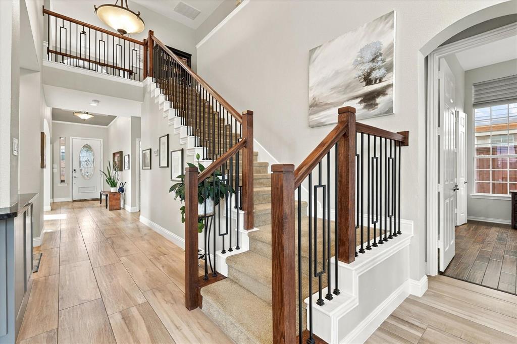 Foyer featuring wood-finish flooring, a staircase with a stained wood handrail, and decorative matte black iron balusters