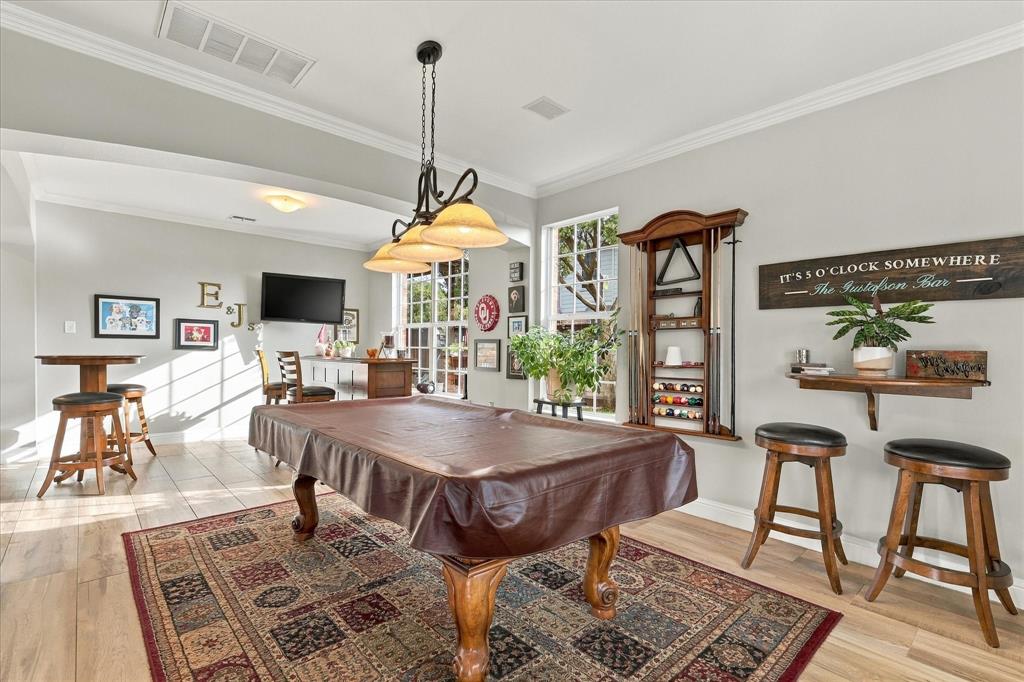 Open-concept area featuring wood-finish flooring, multi-light chandelier with glass shades, tall multi-pane windows, and crown molding