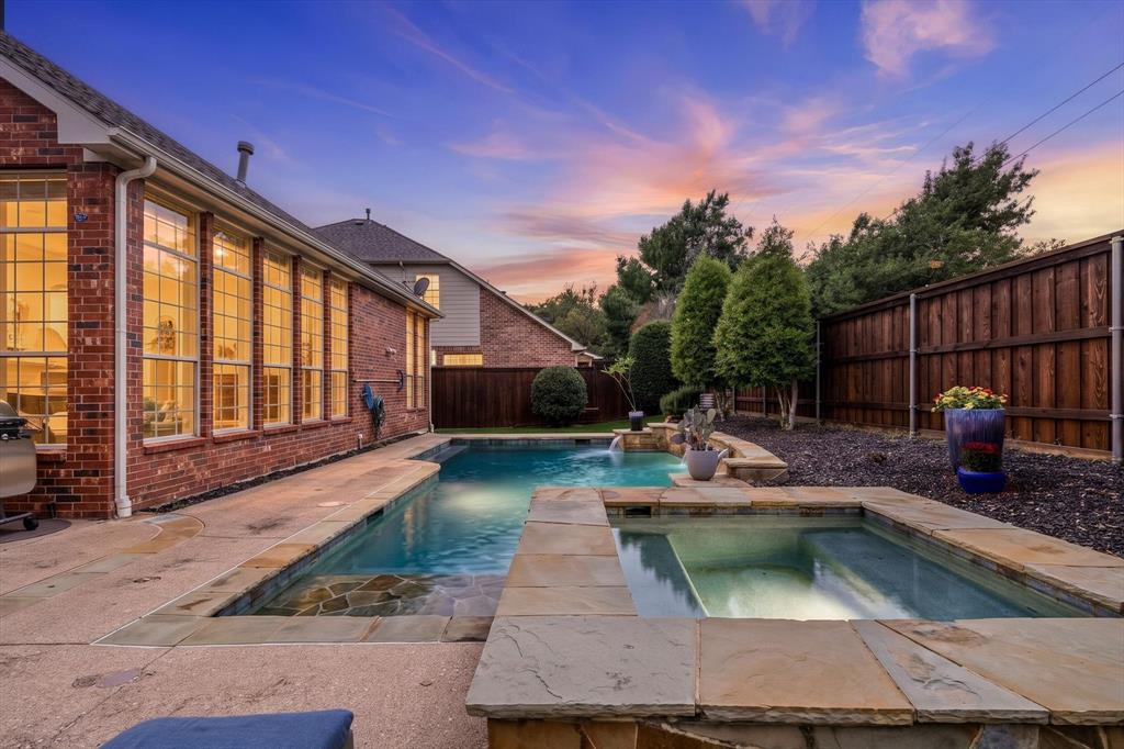 Brick exterior featuring a built-in swimming pool and raised stone spa with integrated water feature, surrounded by a concrete deck and wood privacy fencing