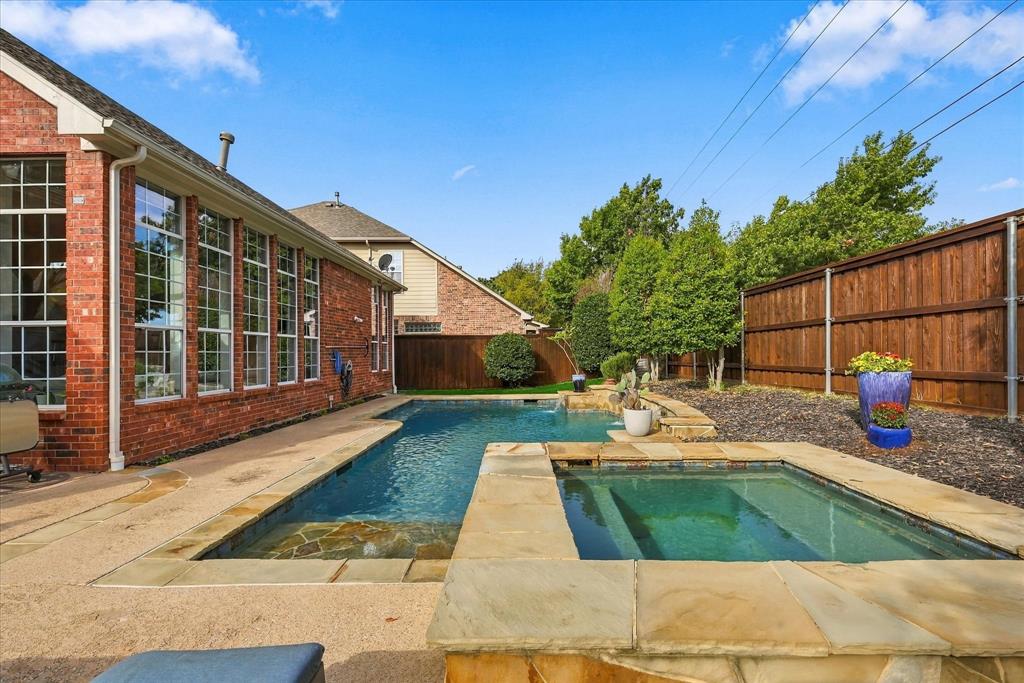 Brick exterior featuring large windows, stone-paved patio, in-ground pool, and built-in stone spa
