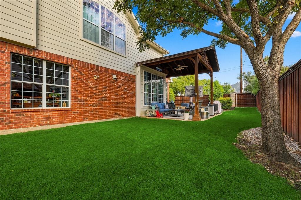 Backyard featuring a covered patio with a ceiling fan, brick and siding exterior, manicured lawn, and mature tree
