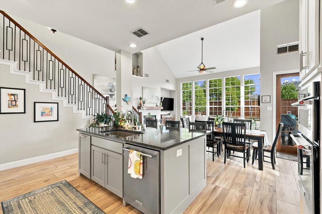 Open-concept kitchen featuring an island with a stone countertop and under-mount sink, wood-finish flooring, vaulted ceilings, and a staircase with a decorative metal railing