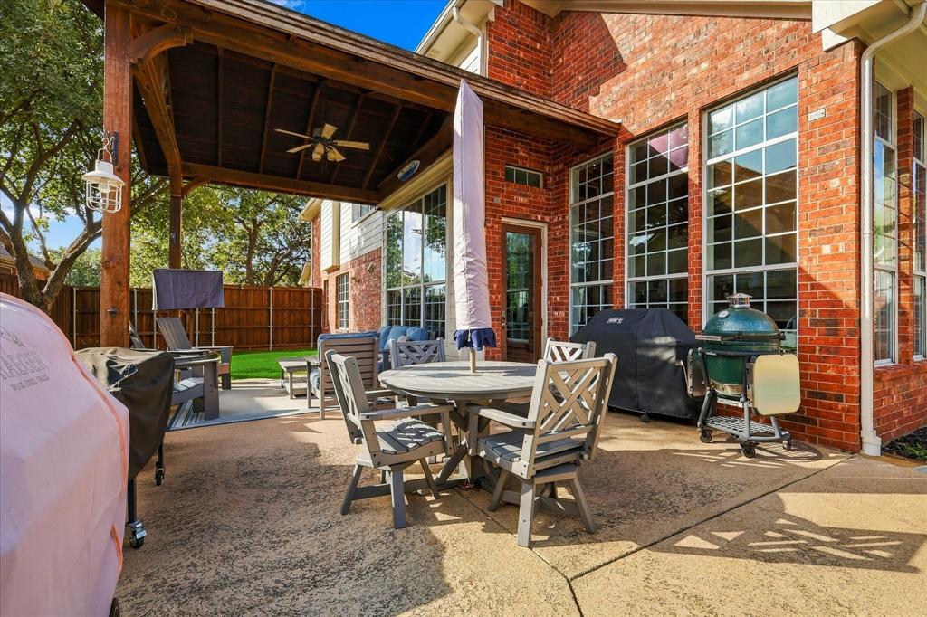 Covered outdoor patio featuring a stained-wood tongue-and-groove ceiling with a mounted ceiling fan, red brick exterior, large grid-pane windows, and concrete hardscaping