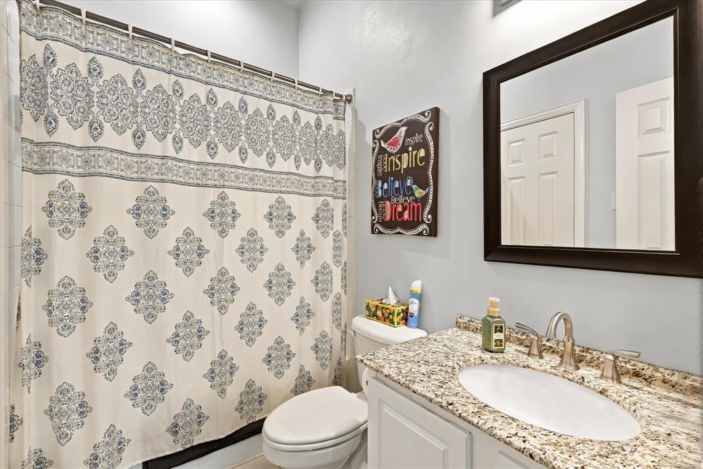 Bathroom featuring a stone-look countertop with an integrated oval basin, brushed nickel widespread faucet, white cabinetry, and a dark-toned framed mirror