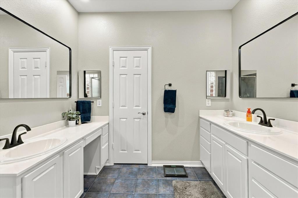 Dual vanity featuring white cabinetry, solid-surface countertops, integrated porcelain sinks, matte black fixtures, and expansive wall-mounted mirrors