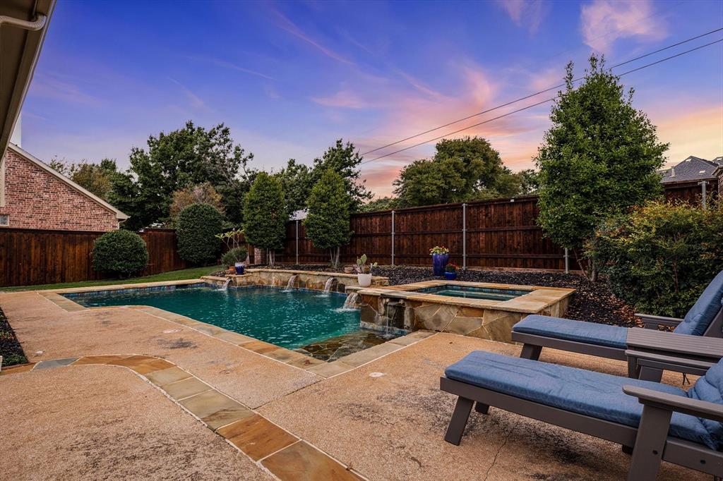 Outdoor space featuring an inground pool with tiered stone water features, integrated spa, decorative stone decking, and a perimeter privacy fence