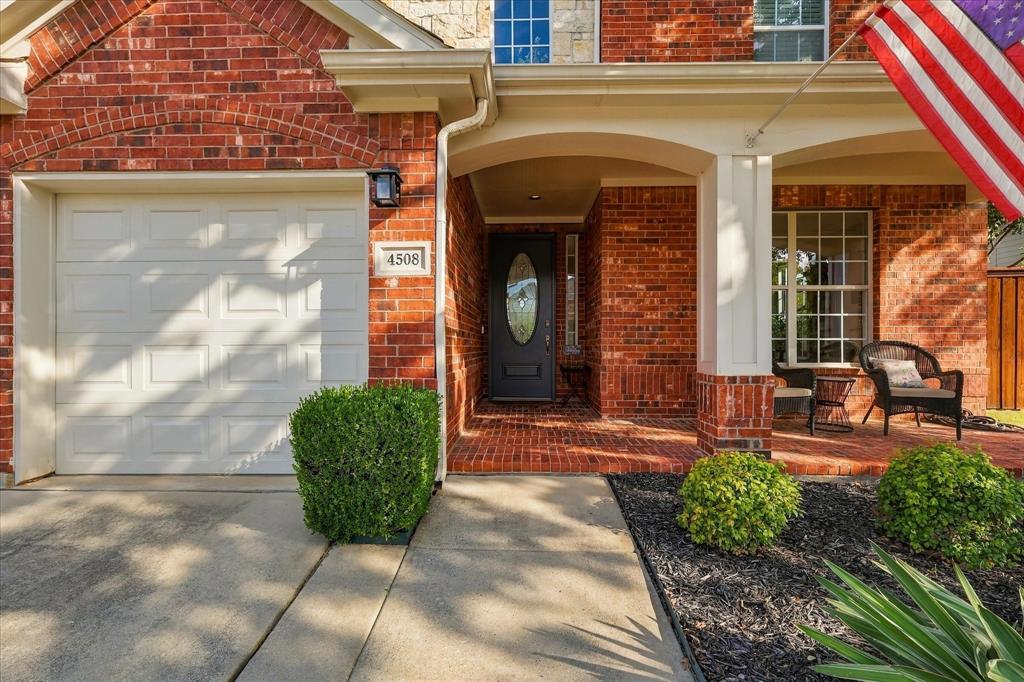Red brick facade featuring a covered front porch with arched architecture, a solid entry door with an oval glass insert, and an attached multi-panel garage door