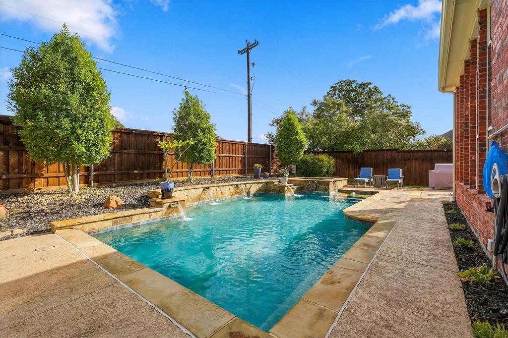 Private backyard featuring an in-ground swimming pool with water features, natural stone coping, concrete decking, and perimeter wood fencing