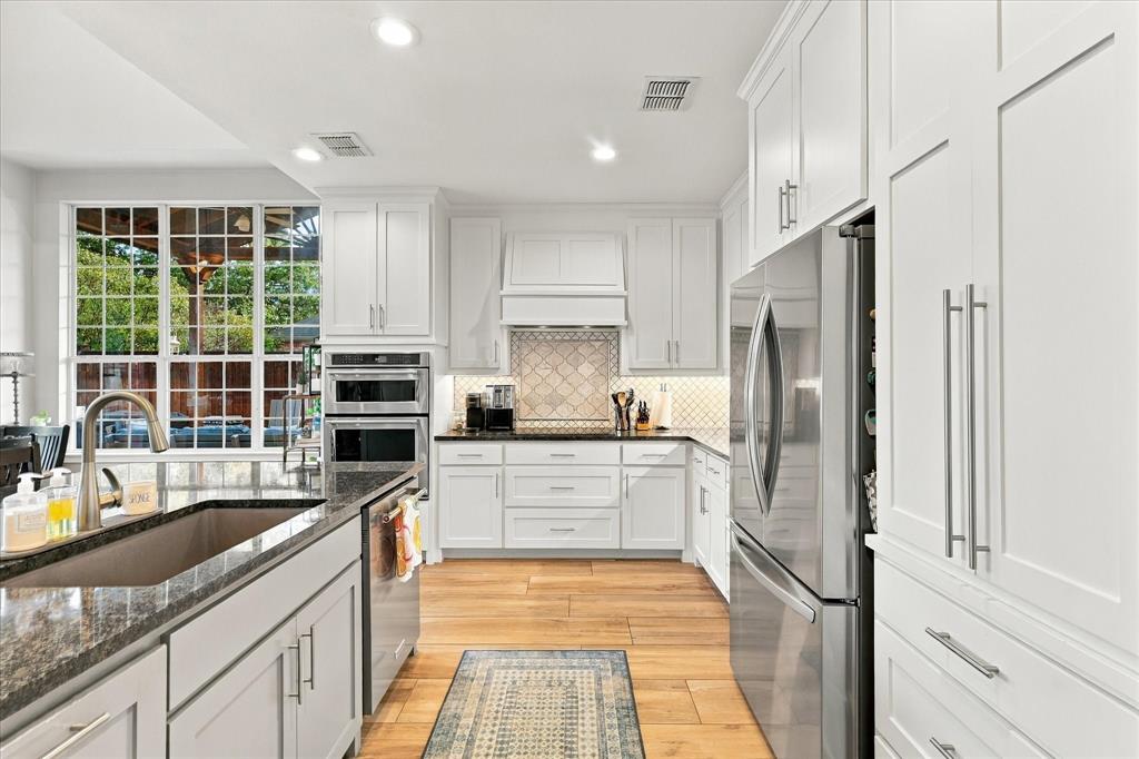 Kitchen featuring white cabinetry, wood-finish flooring, dark stone countertops, stainless steel appliances, and a tiled backsplash