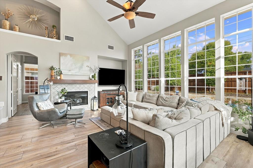 Living area featuring vaulted ceilings, wood-finish flooring, a fireplace with a decorative tile surround and wood mantel, built-in display niche, and floor-to-ceiling windows