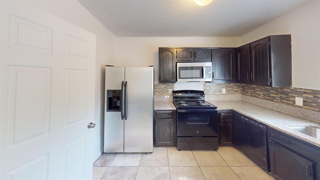 Kitchen featuring dark wood cabinetry, light-toned countertops, a mosaic tile backsplash, a stainless steel refrigerator, and a built-in microwave