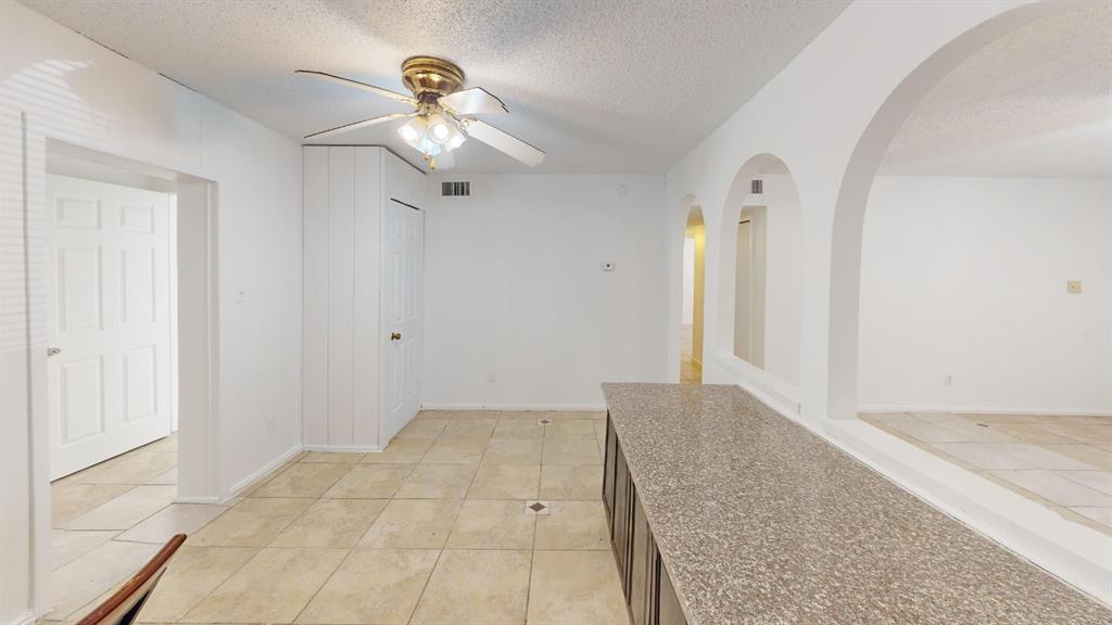 Tile flooring, built-in cabinetry with a stone-finish countertop, arched room openings, and a ceiling fan with integrated lighting