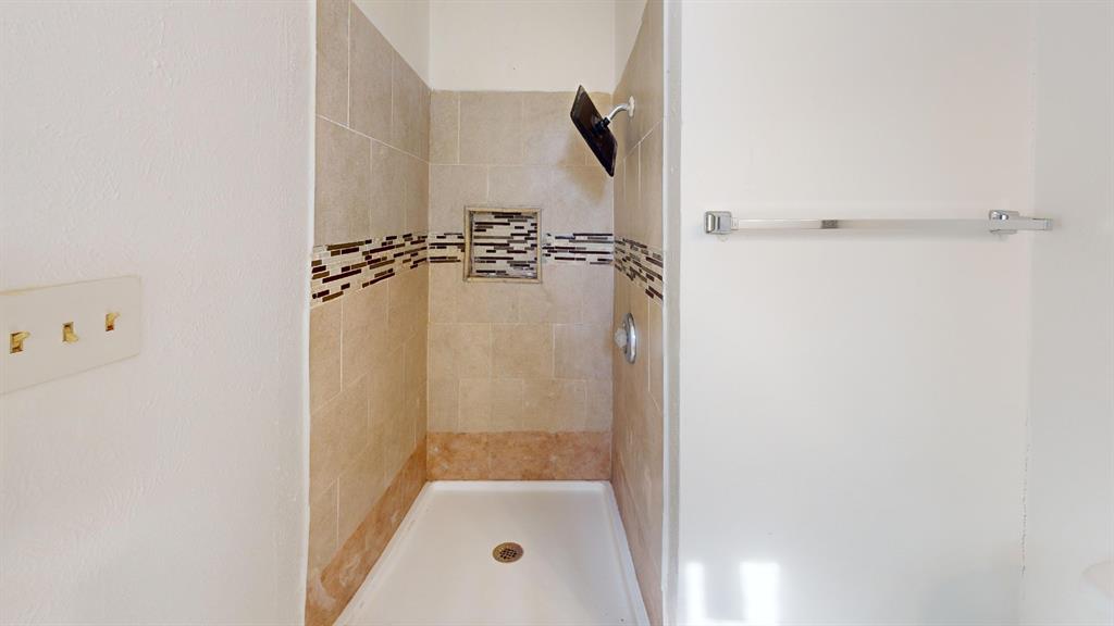 Tiled shower stall featuring a built-in niche, decorative accent band, and a single-handle shower fixture