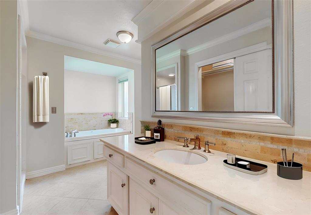 Spa-inspired primary bathroom featuring dual vanities with white cabinetry, a quartz countertop, and brass fixtures