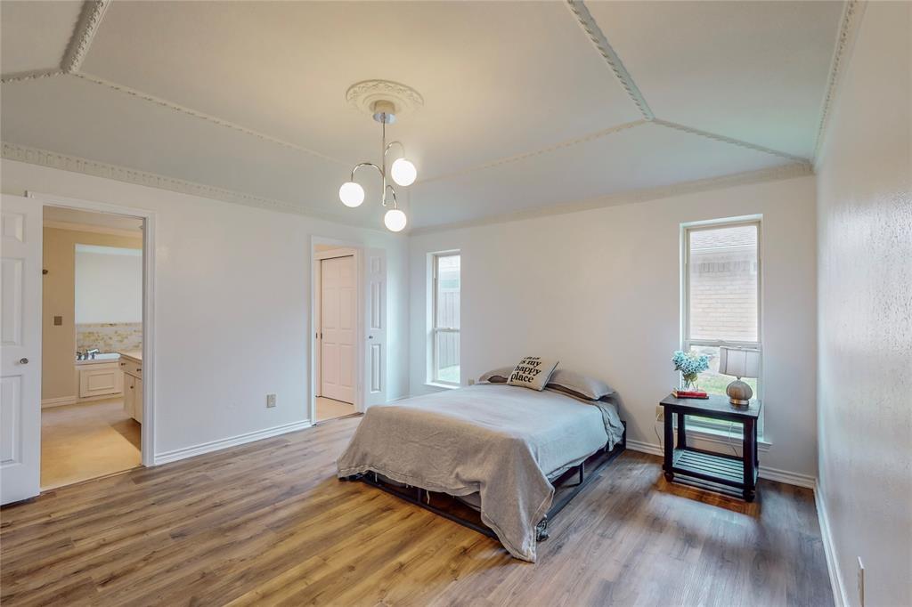 Wood-finish flooring, recessed ceiling with decorative molding, contemporary chandelier, and multiple windows with roller shades