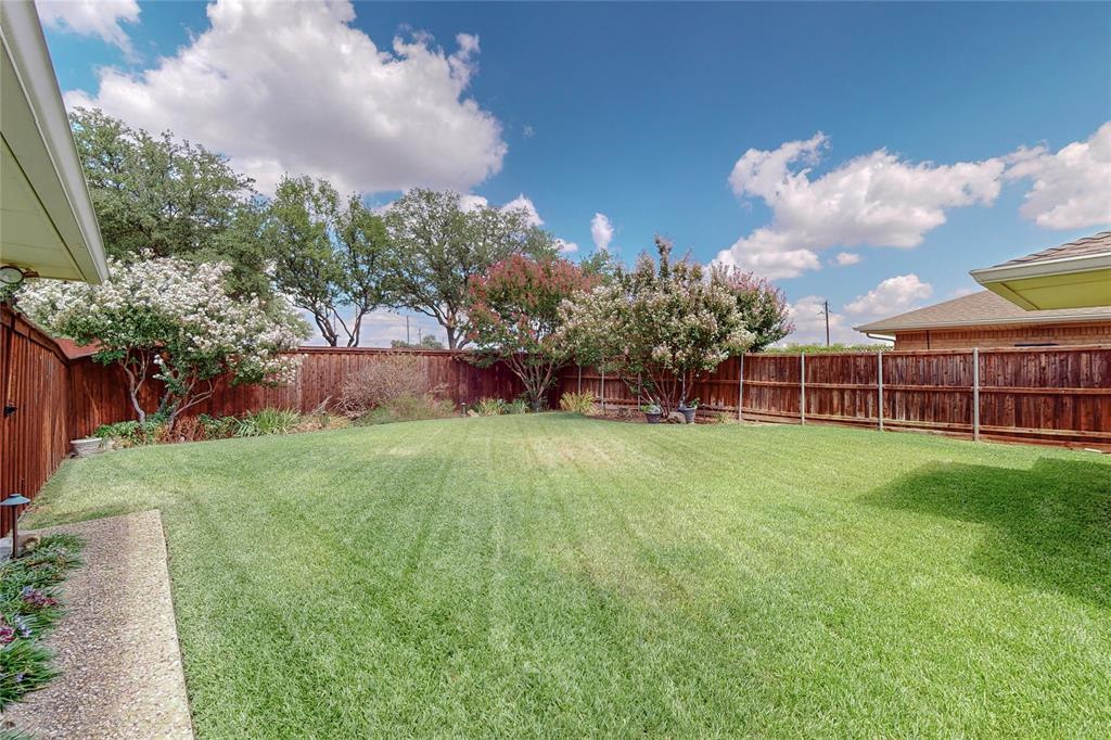 Expansive lawn area with a perimeter wood privacy fence, mature trees, and flowering shrubs