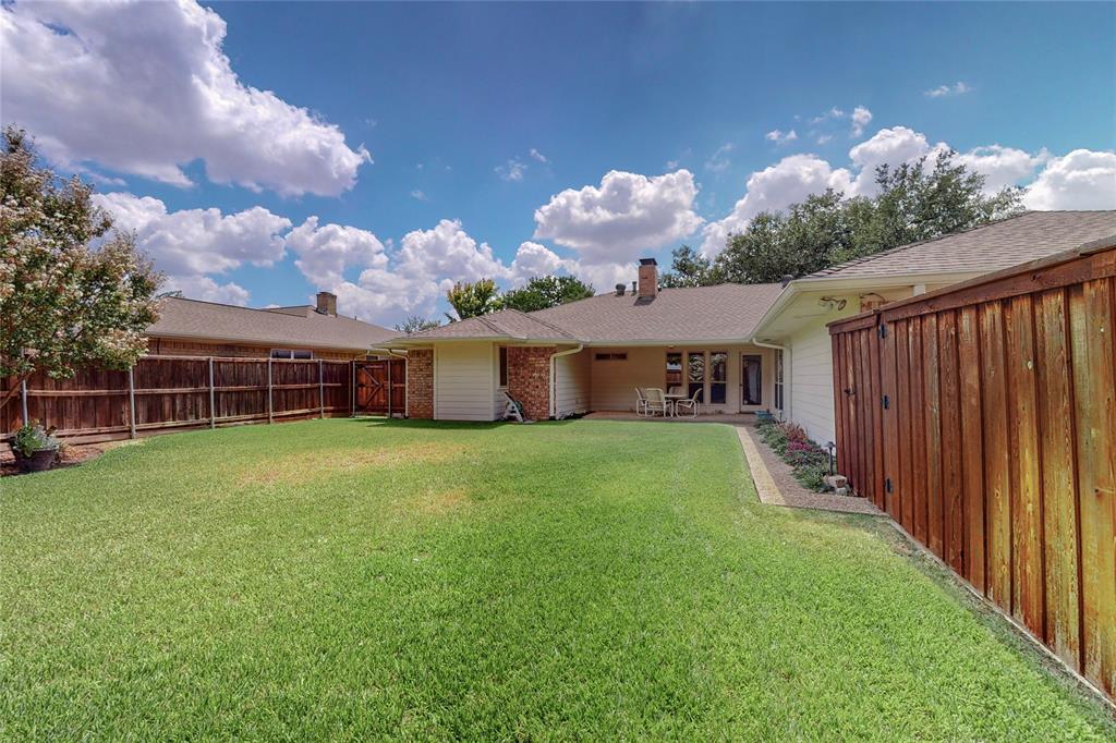 Expansive backyard with a large lawn area, wood privacy fencing, and a paved patio area